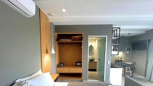 Una habitación de hotel moderna con una cama, un armario, un baño con lavabo y espejo, y una pequeña zona de kitchenette.