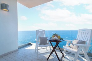 A balcony with two white chairs, a small table with a tray of items, and a view of the sea.