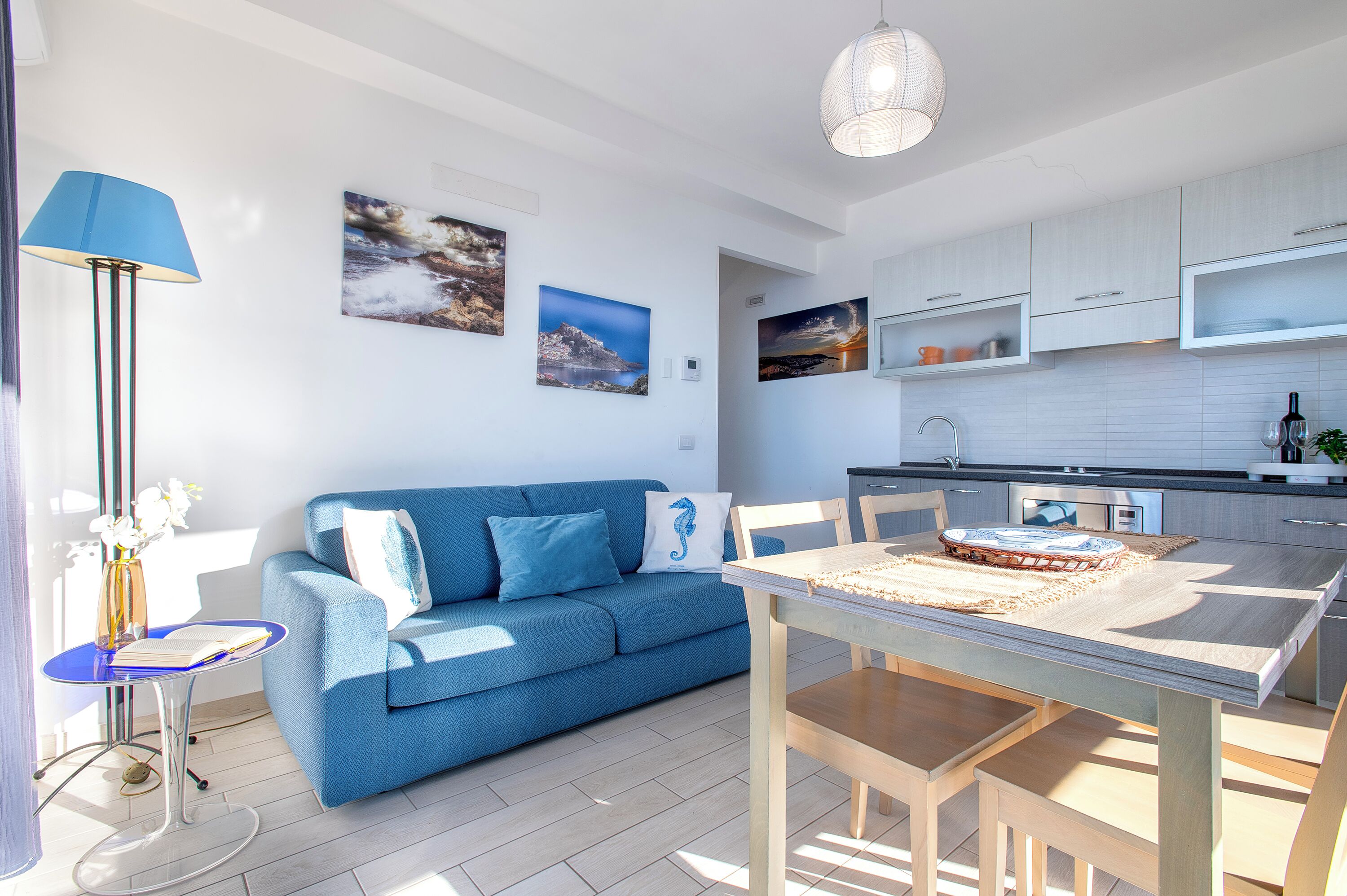 A modern living room with a blue sofa, a dining table, and a kitchen area.