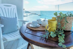 A balcony with a white chair, a wooden table with a woven placemat, and a view of the sea.