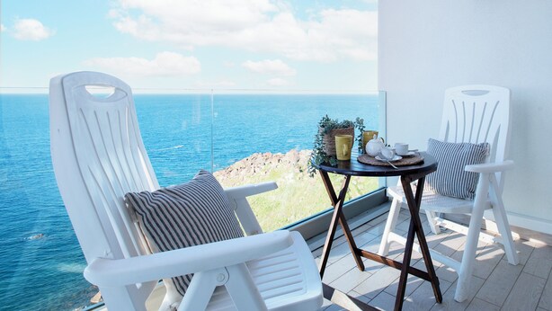 A balcony with two white chairs, a small round table with a plant, and a view of the sea. - Sardinia Re - Miramare 14 Sea View (Castelsardo)