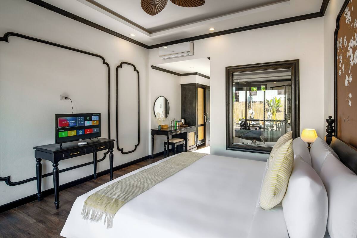 A modern hotel room with a large bed, a desk with a computer, a mirror, and a view of the outdoors.