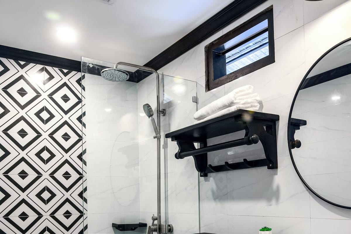 A modern bathroom with a geometric patterned floor, a white toilet, a black sink, and a shower with a handheld showerhead.