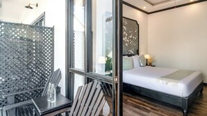 A modern hotel room with a large bed, a wooden table with two bottles, a chair, and a large window with a view of the city. - Vang Luang Hotel (Luang Prabang)