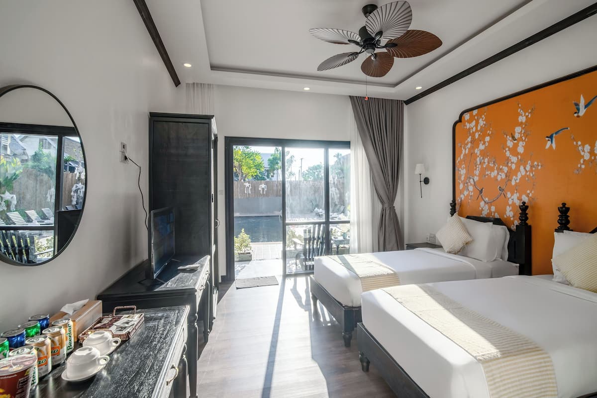 A hotel room with two beds, a desk with a mirror, a ceiling fan, and a view of the outside.