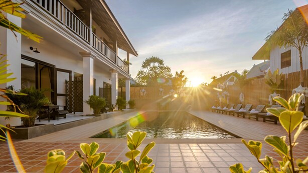 A pool area with a view of a building with a balcony, surrounded by plants and a clear sky. - Vang Luang Hotel (Luang Prabang)