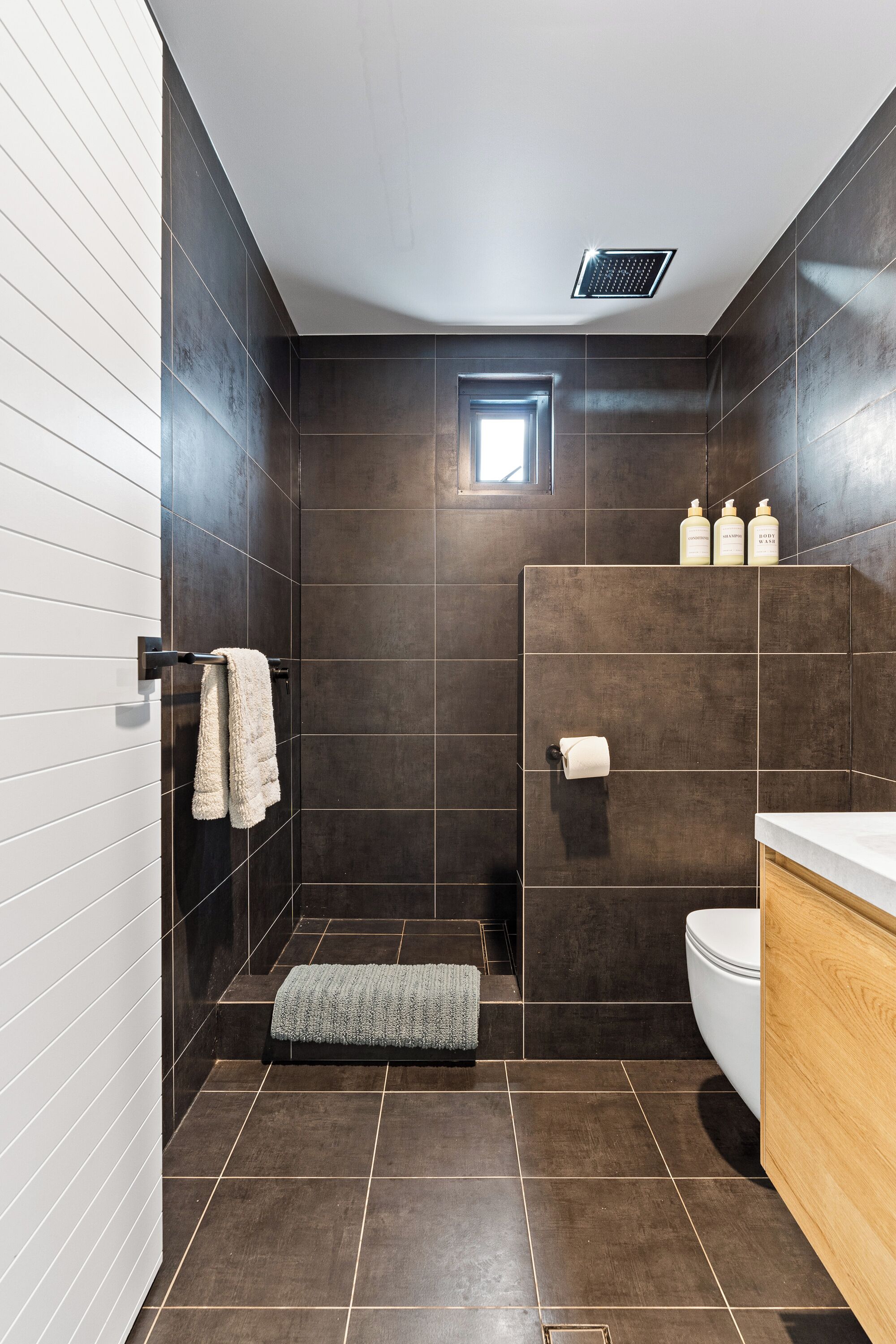 Une salle de bain moderne avec des carreaux foncés, un lavabo blanc et un meuble-lavabo en bois.