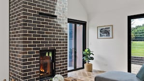 A modern living room with a brick fireplace, wooden flooring, a grey sofa, and a wooden coffee table. - The Mist, Luxury Farm Retreat w/ Fireplace & Hot tub | Southern Highlands (Exeter)