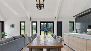 A spacious dining area with a long wooden table, grey upholstered seating, and a view of the outdoors. - The Mist, Luxury Farm Retreat w/ Fireplace & Hot tub | Southern Highlands (Exeter)