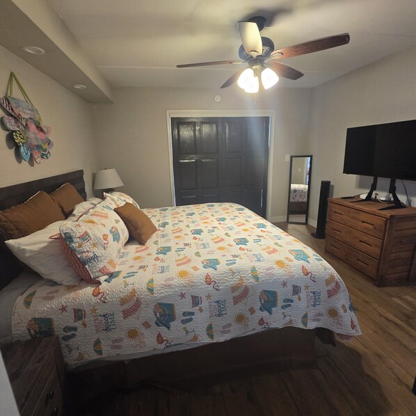 Une chambre à coucher avec un lit, un ventilateur de plafond, une commode, un miroir et un téléviseur.