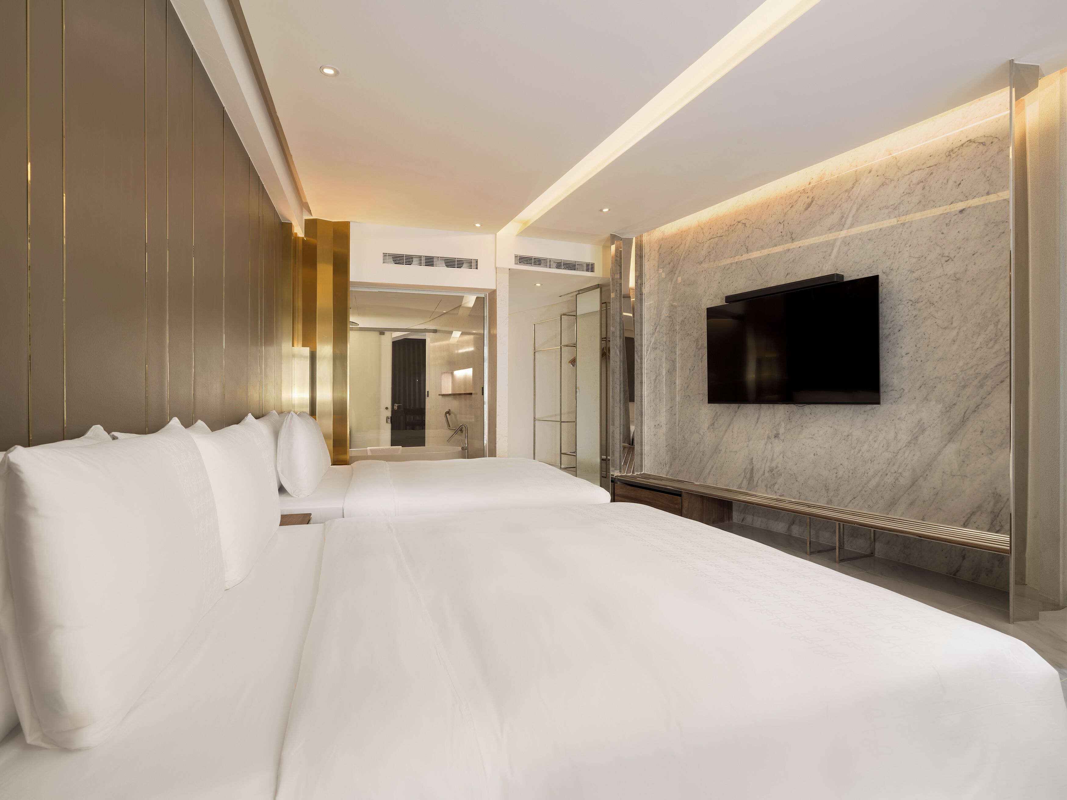Una habitación de hotel moderna con una cama grande, un televisor montado en la pared y una zona de ducha con paredes de cristal.
