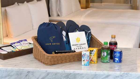 Quarto de hotel com cama, cesta de vime com artigos de higiene pessoal, garrafa de Coca-Cola, lata de Fin e caixa de suco de laranja.