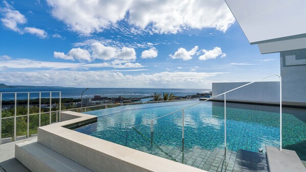 A clear blue sky with clouds, a swimming pool with clear water, and a view of the ocean and distant buildings. - Orient Luxury Hotel-KenTing (Hengchun)