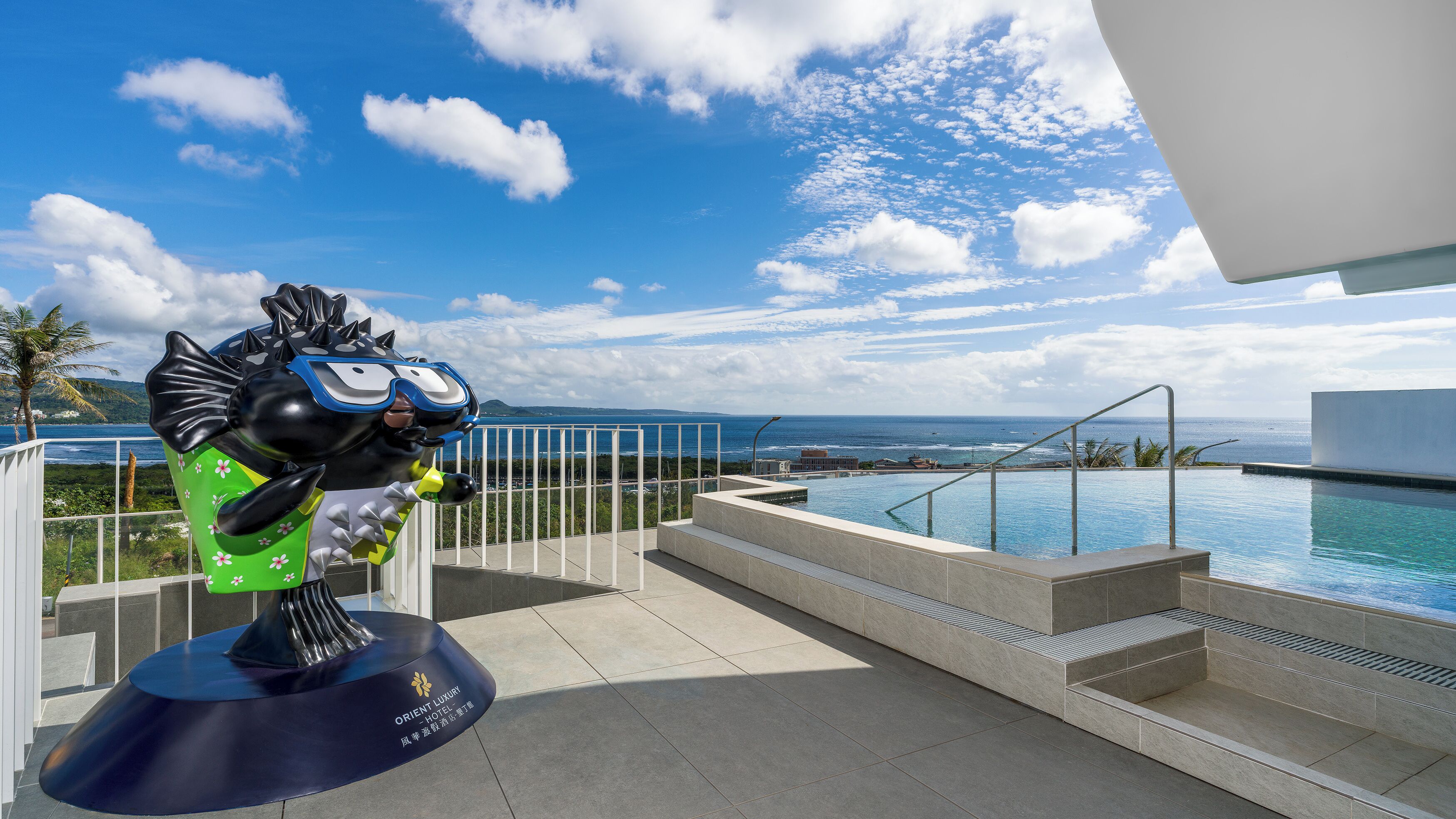 A modern hotel with a pool, a statue, and a view of the ocean.