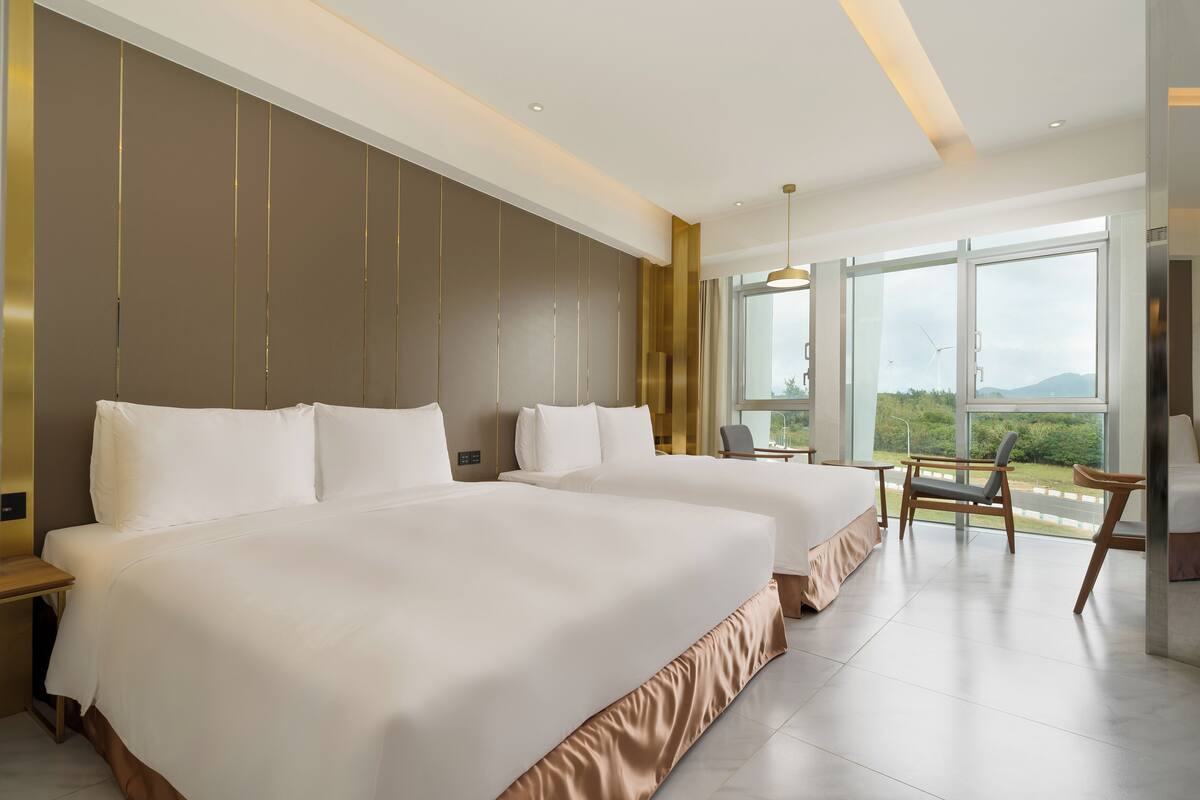A hotel room with two beds, a large window, and a view of the outdoors.