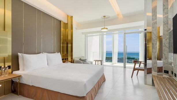 A modern hotel room with a large bed, a desk, a chair, and a view of the ocean. - Orient Luxury Hotel-KenTing (Hengchun)