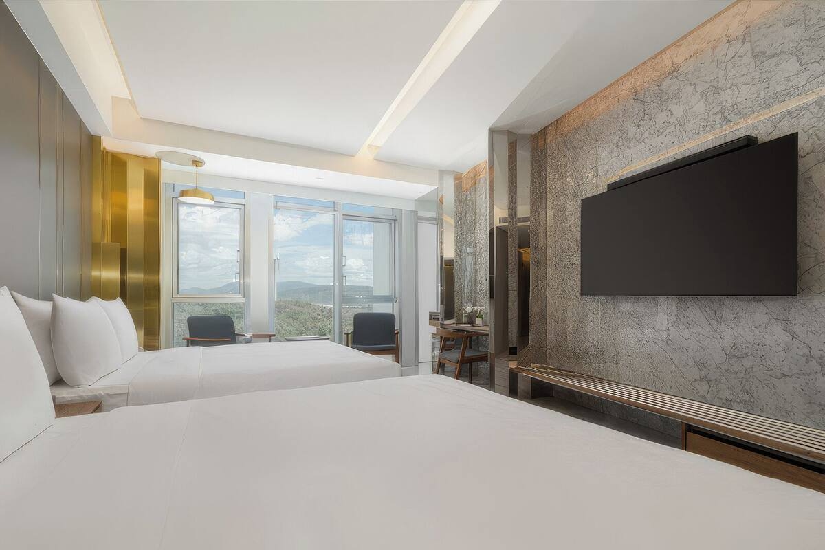 A modern hotel room with a large bed, a TV mounted on the wall, and a view of the outdoors.