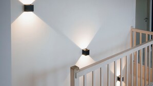 Una escalera con barandillas de madera y una pared blanca con dos luces empotradas.