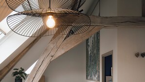 Un dormitorio estilo loft moderno con techo inclinado, una escalera de madera, un rincón de descanso acogedor y una mesa de comedor con una planta y una revista.