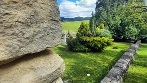 A stone wall, a paved path, and a grassy area with trees and a distant view of hills. - Harmónia Wellness Villa (Szilvasvarad)