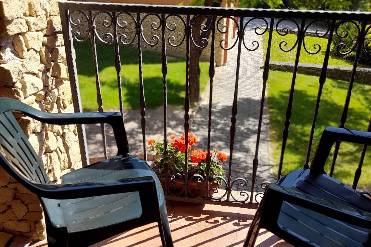 Un patio con dos sillas negras, un muro de piedra y una barandilla de metal con una maceta.