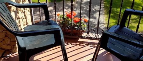 A patio with two black chairs, a stone wall, and a metal railing with a flower pot.