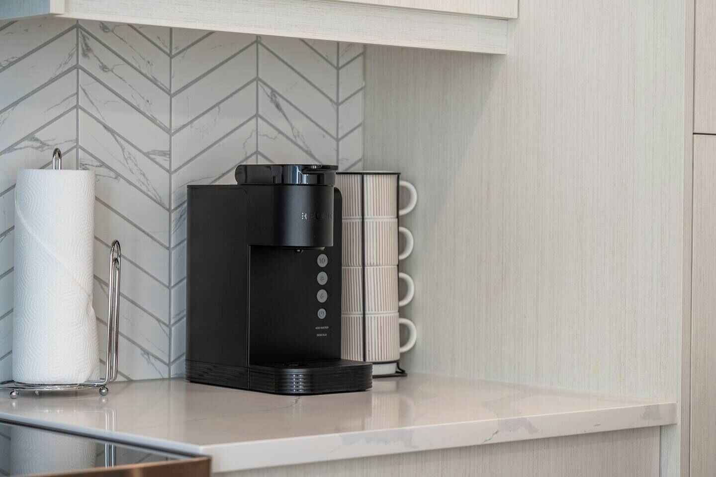 A modern kitchen with a black coffee machine, a paper towel holder, and a white marble countertop.