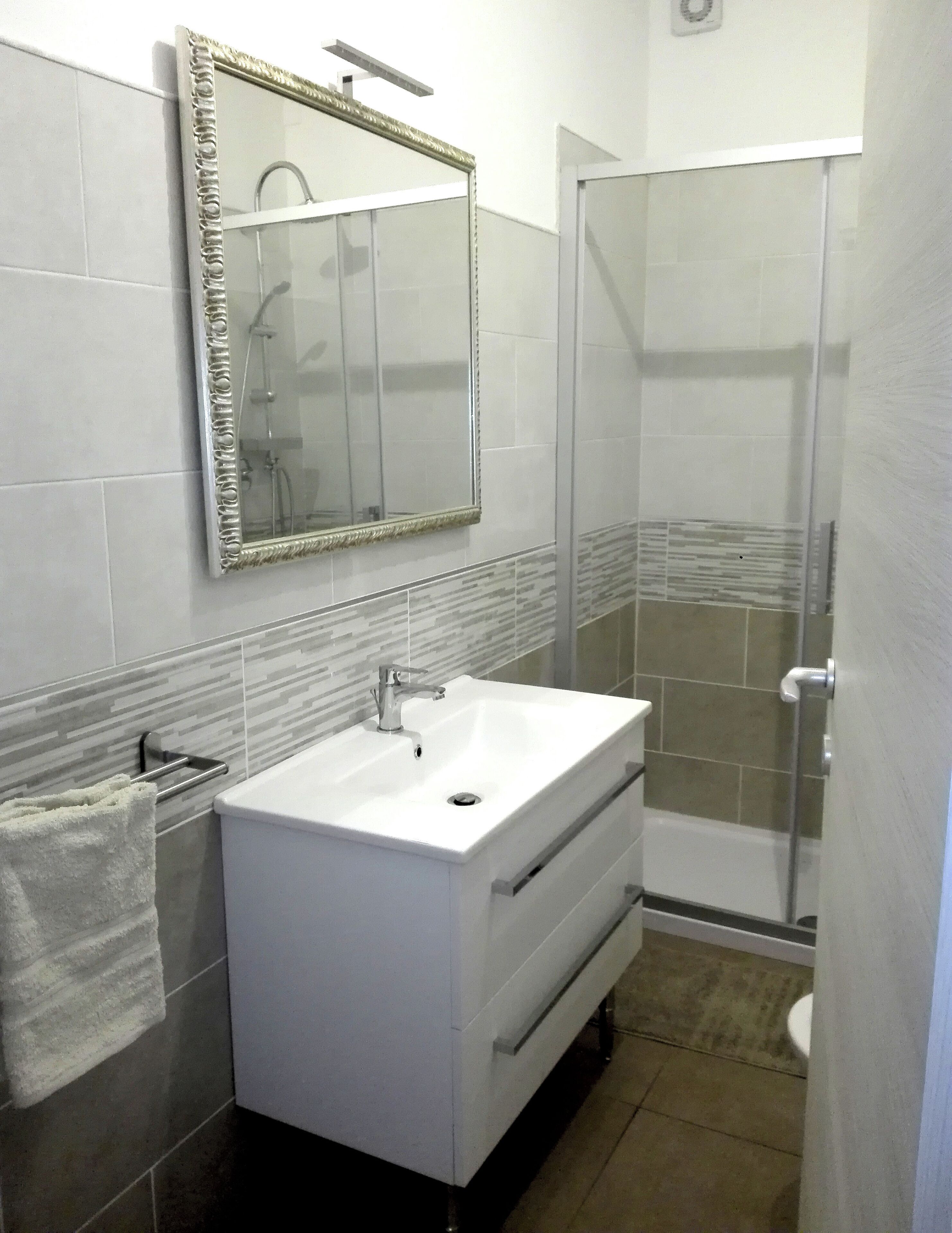 Un baño con lavamanos blanco, un espejo con marco dorado y una zona de ducha.