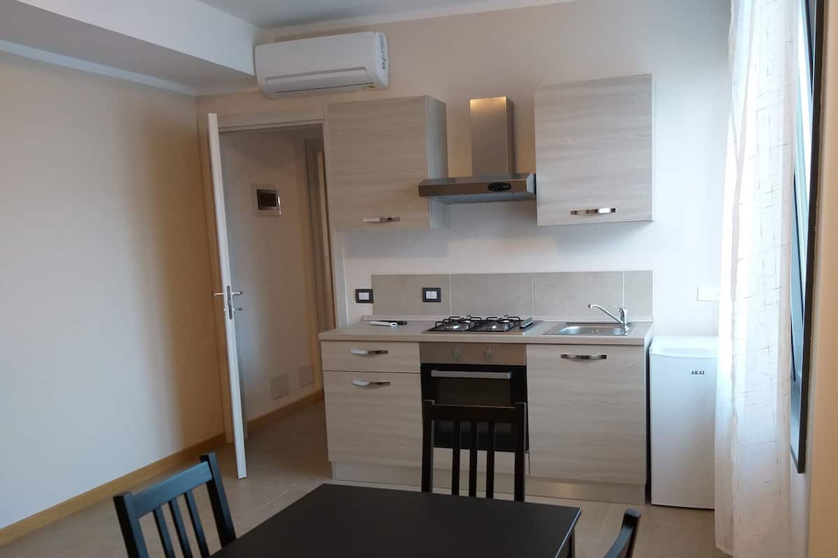 A compact kitchen with a stove, sink, and a small refrigerator. There is a dining table with chairs.