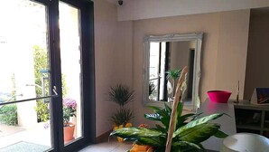 A hotel lobby with a sliding glass door leading to a balcony, potted plants, a mirror, and a white cabinet with a magazine. - appartamenti la piazzetta (Signa)