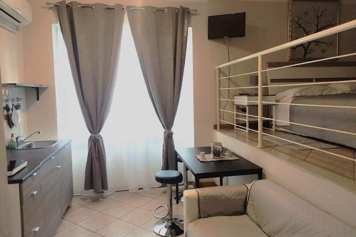 A compact hotel room with a kitchenette, a sofa, a small table, a TV, and a bunk bed.