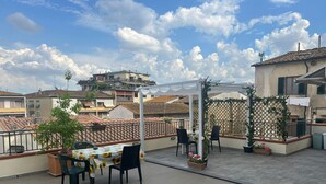 A rooftop patio with a table and chairs, surrounded by potted plants and a pergola. - appartamenti la piazzetta (Signa)