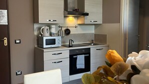 A modern kitchen with stainless steel appliances, a built-in oven, and a microwave. There is a small dining area with a white table and chairs. - appartamenti la piazzetta (Signa)
