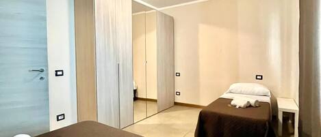 A hotel room with two beds, a large mirror, and a ceiling light.