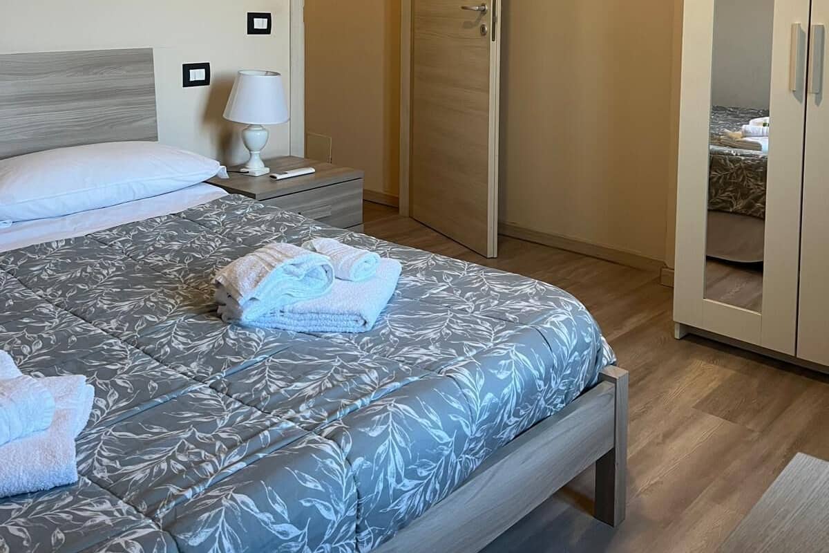 A bedroom with a bed, a nightstand, a lamp, an air conditioner, and a wardrobe.