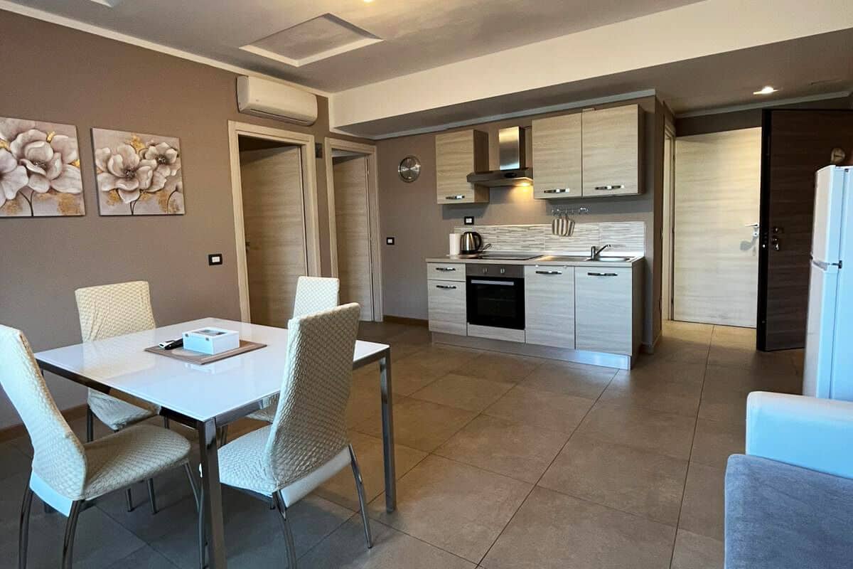 A modern kitchen with white cabinets, a dining area with a white table and chairs, and a living area with a blue sofa.