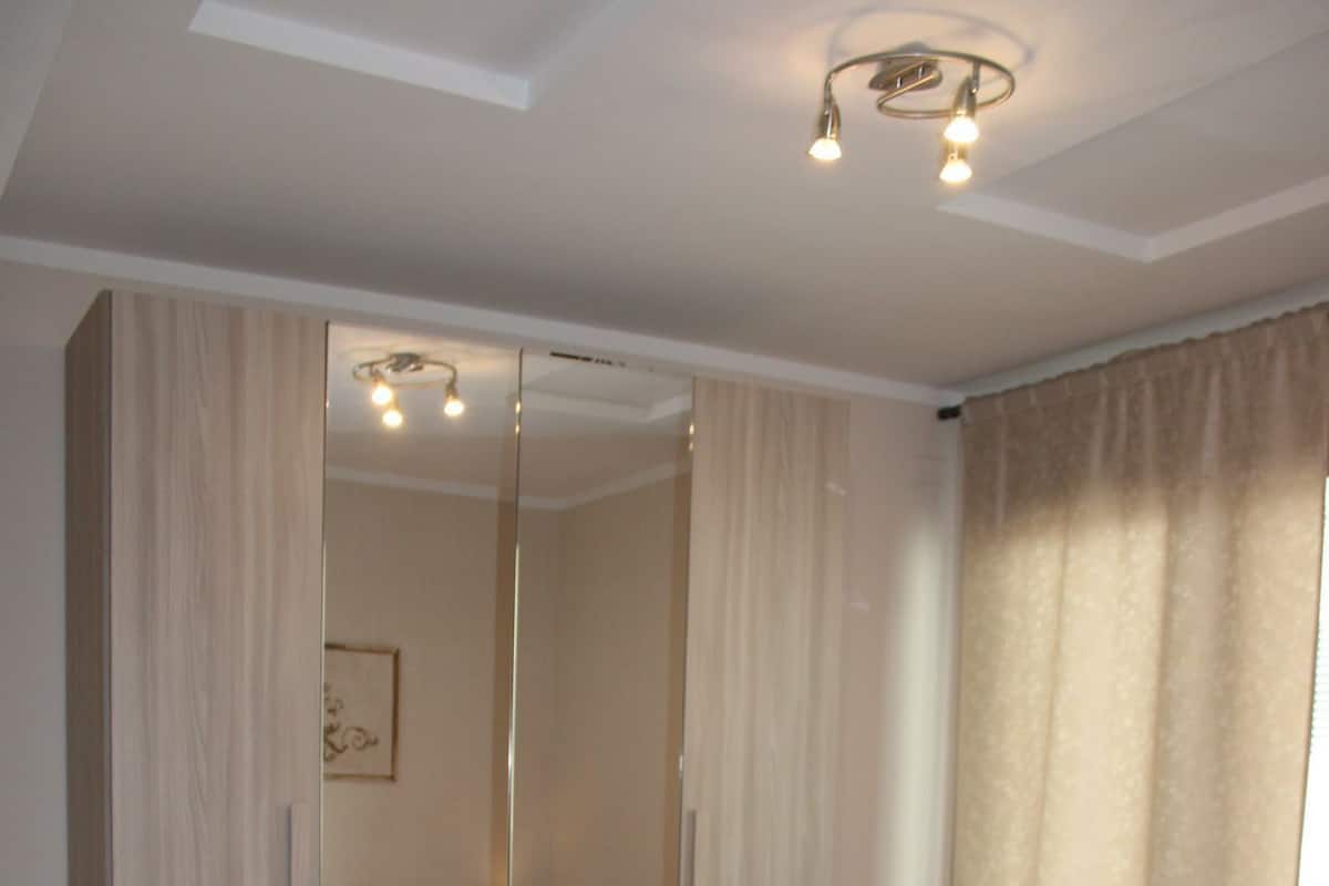A bedroom with a bed, a mirror, and a window with curtains.