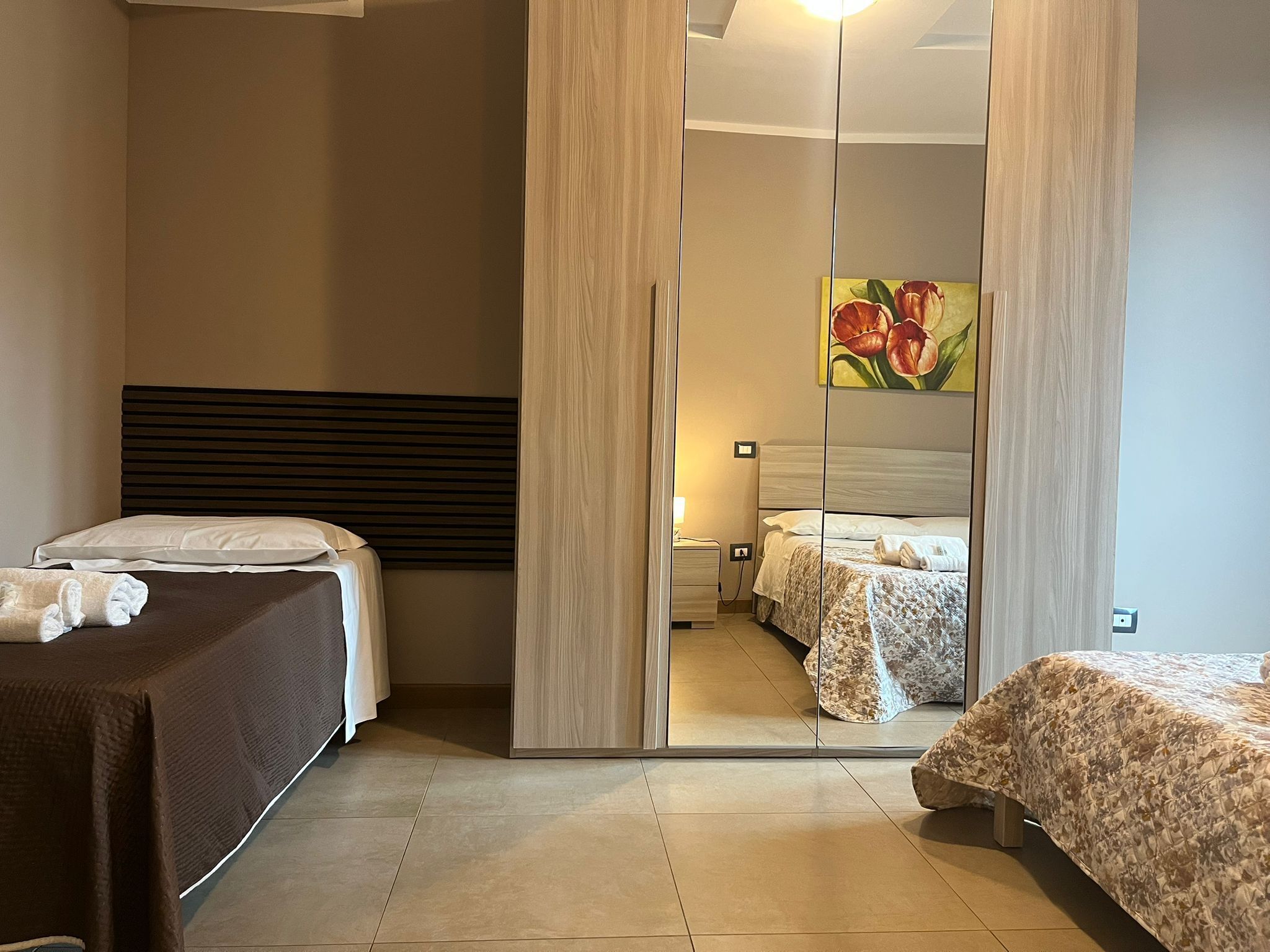 Ein Hotelzimmer mit einem großen Spiegel, zwei Betten, einem hölzernen Kopfteil und einem Blumenbild.