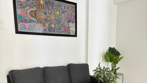 Un salon avec un canapé gris, une table basse en bois sur laquelle repose un journal, et un grand tableau abstrait et coloré accroché au mur.