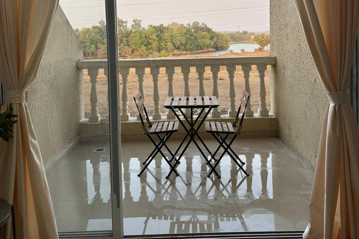 Varanda com mesa e cadeiras, vista para vegetação e um corpo d'água, e um corrimão.