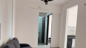 Un vaste espace de vie avec un canapé aux couleurs sombres, un ventilateur de plafond et une vue sur une autre pièce.
