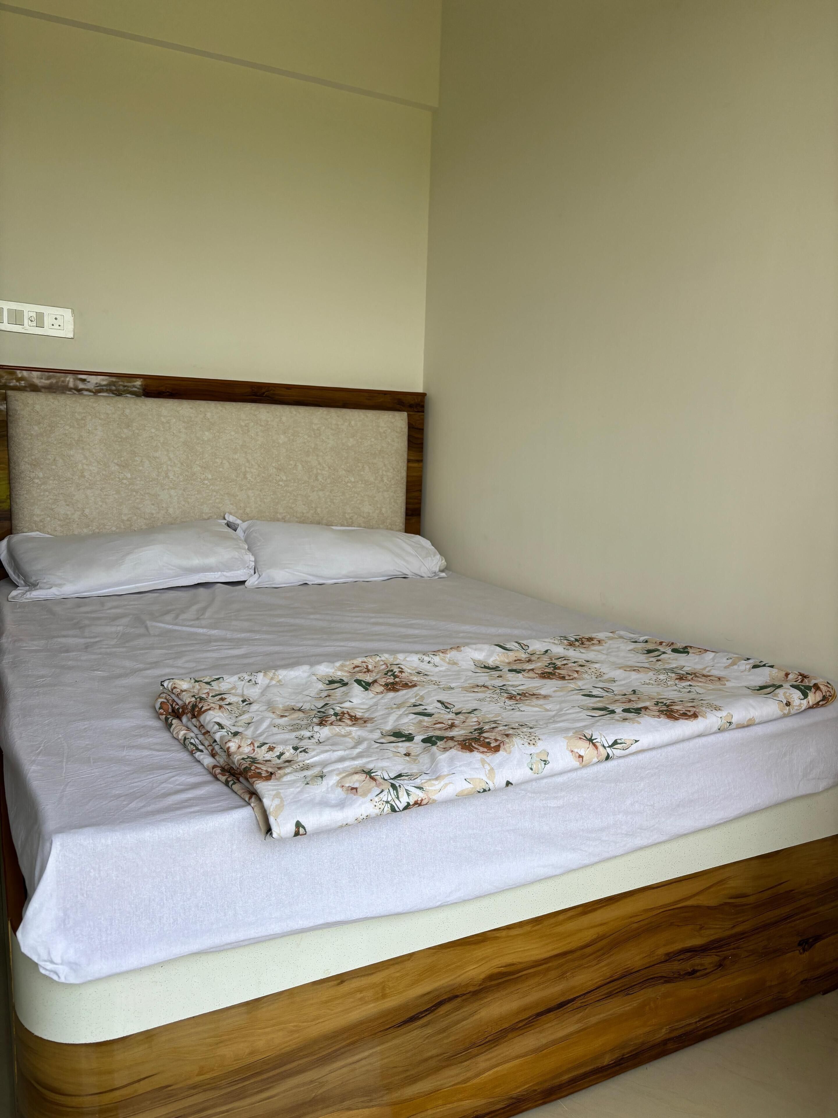 A bed with a wooden headboard, white bedding, and a floral-patterned blanket.