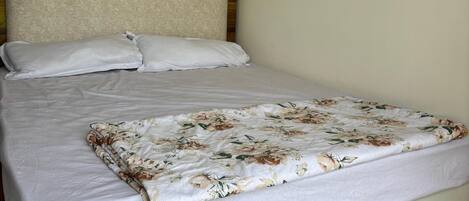 A bed with a wooden headboard, white bedding, and a floral-patterned blanket.
