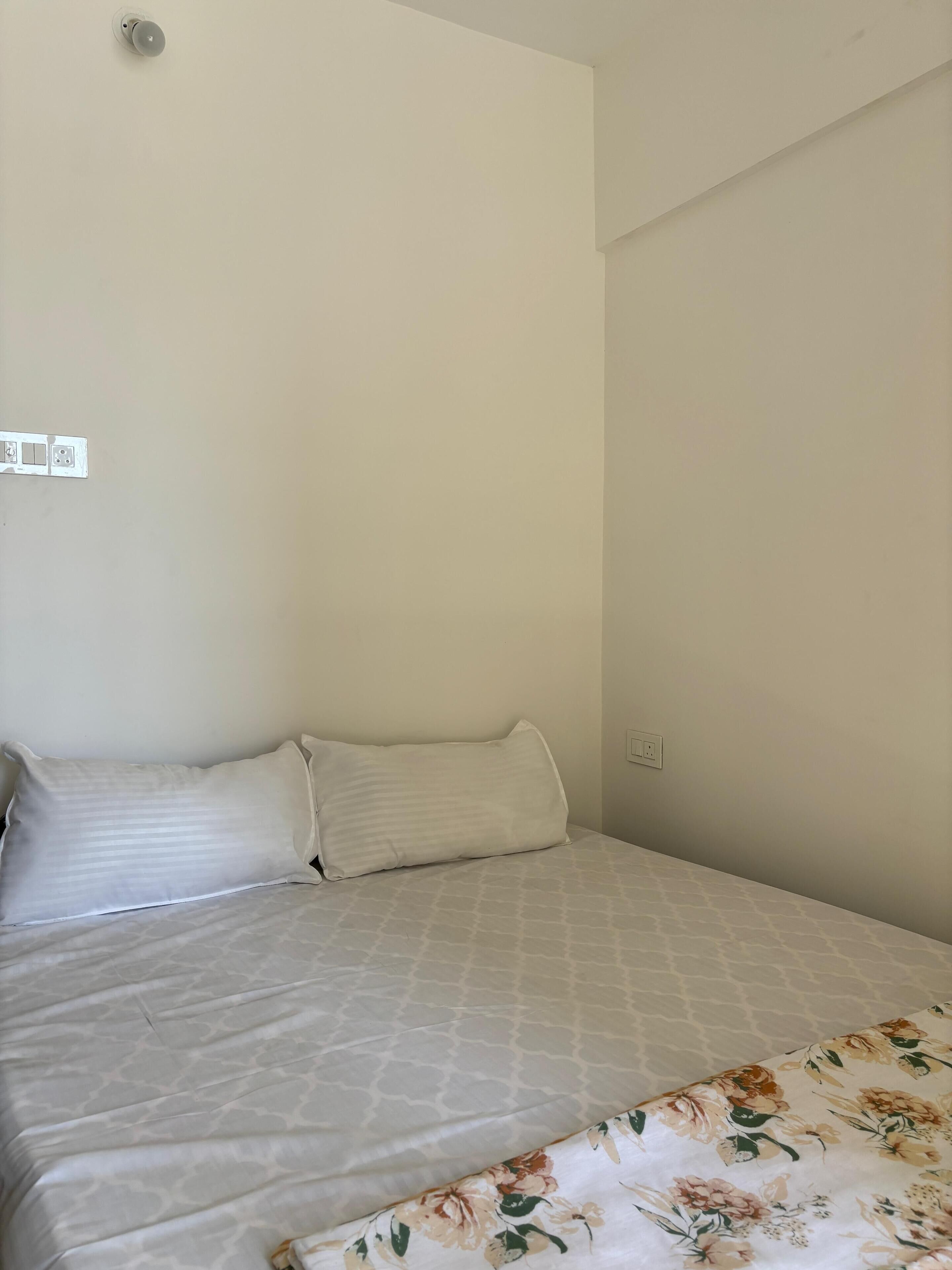 A simple, clean room with a bed, a power outlet, and a light switch on the wall.