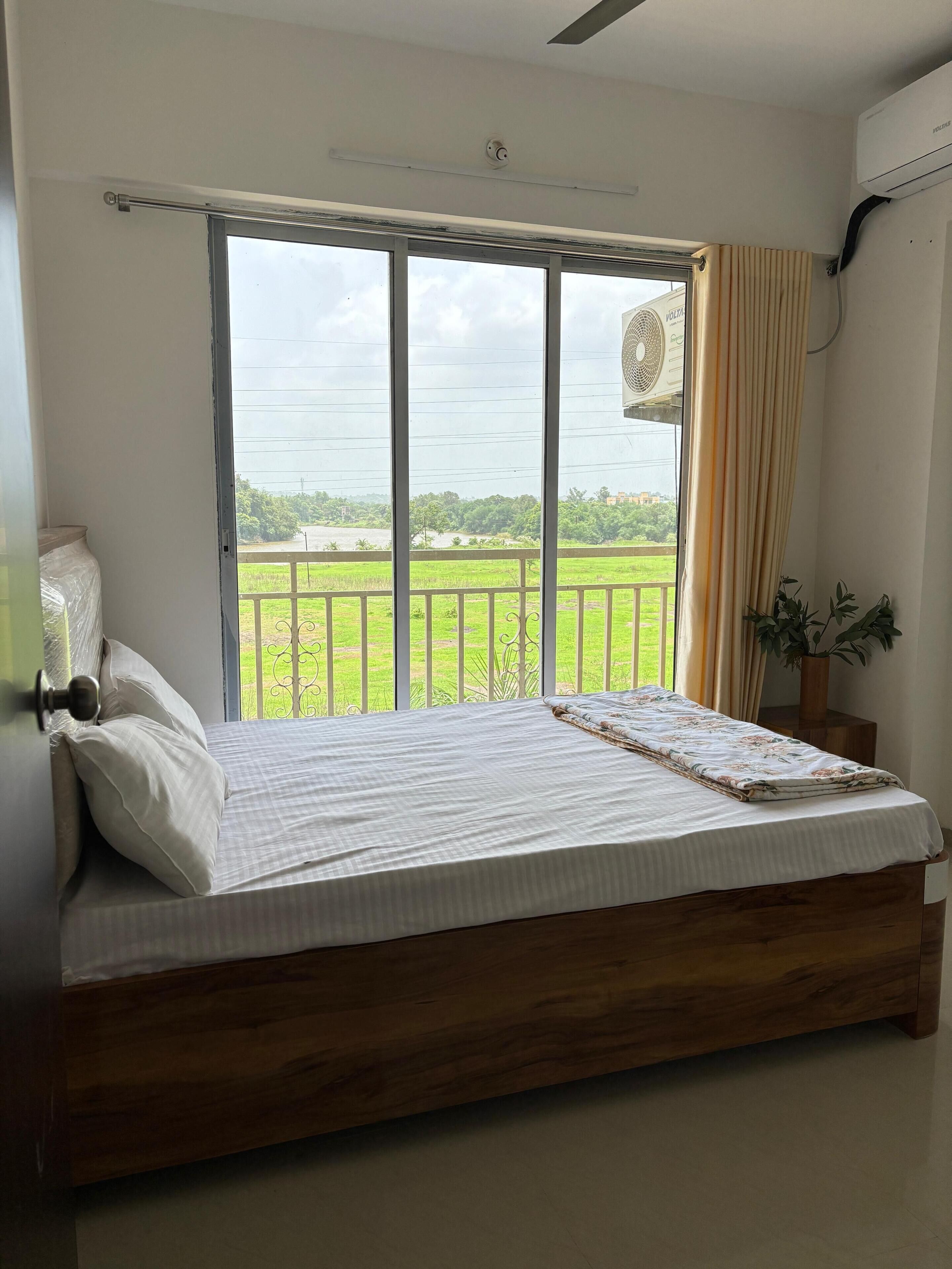 Une chambre dotée d’un grand lit, offrant une vue sur un paysage verdoyant grâce à une porte coulissante, et comprenant un climatiseur fixé au mur.