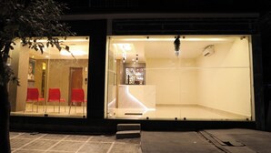 A hotel entrance with a reception desk, a waiting area with red chairs, and a glass partition. - Hotel Green Parrot (Madurai)