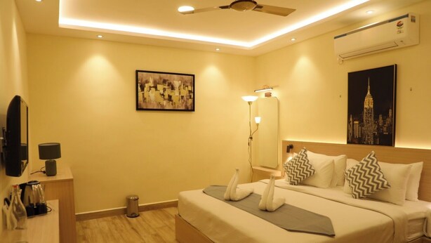 A hotel room with a bed, bedside table, lamp, mirror, and artwork on the walls. - Hotel Green Parrot (Madurai)