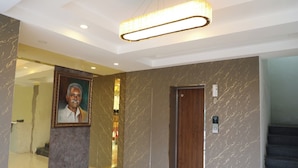 A lobby with marble walls, a framed portrait, a wooden door, and a staircase. - Hotel Green Parrot (Madurai)