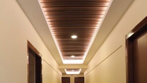 A hallway with a wooden ceiling and recessed lighting, leading to a door at the end. - Hotel Green Parrot (Madurai)