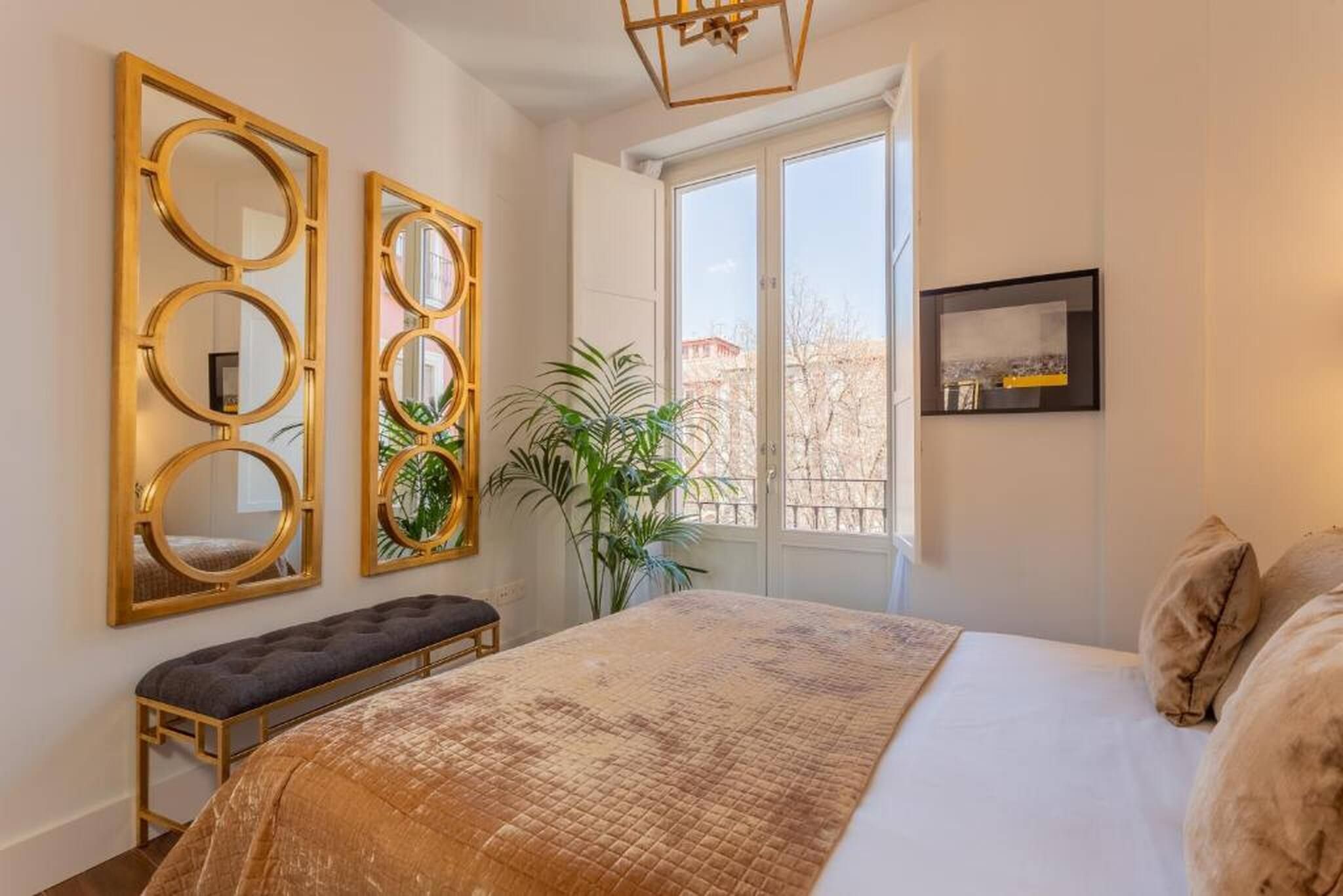 Quarto com uma cama grande, um banco e três espelhos fixados na parede.
